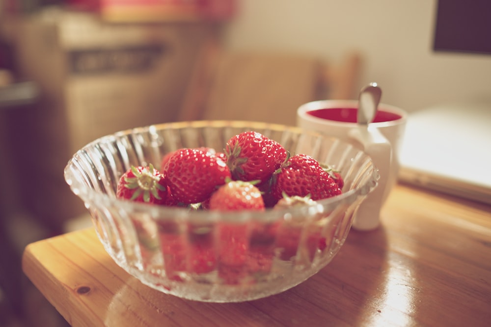 bowl of strawberries beside white mug on table